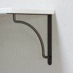 a white shelf with black metal brackets on the top and bottom, against a white wall