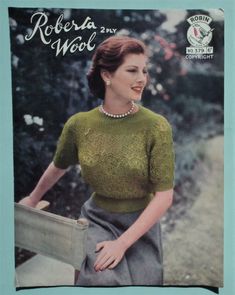 a woman wearing a green knitted sweater and skirt with pearls on the collar, standing in front of trees