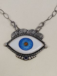 Handmade from scratch Evil Eye Hamsa Cloisonne Enamel Necklace   Handmade by me in my beautiful Kansas City studio. See our work and follow us on Instagram please. Questions and comments are welcome.  Instagram: https://www.instagram.com/anaraandco/ Sterling Silver and Fine Silver necklace is made in glass vitreous Japanese enamel. Setting made out of sterling silver. Front adorned with silver balls, hand stamped design on top, sapphire stone is set in bezel setting, back has a hand sewn hamsa hand. All cut by hand. Soldered, stamped, handsewn, grinded, polished, oxidized.  Vitreous enamel, also called porcelain enamel, it's when material made by fusing powdered glass to a substrate by firing. The powder melts in the special kiln at 1500 degree F, flows, and then hardens to a smooth, durab Handmade Spiritual Enamel Jewelry, White Enamel Bohemian Jewelry, White Bohemian Enamel Jewelry, Hand Painted Sterling Silver Bohemian Jewelry, Handmade Spiritual Enamel Necklaces, Handmade Round Enamel Necklaces, Handmade Enamel Round Necklace, Handmade Enamel Round Necklaces, Handmade Round Enamel Necklace