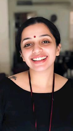 a smiling woman wearing a black shirt and red necklace with a cross on it's neck