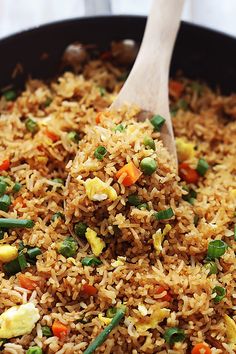 rice and vegetables are mixed together in a skillet with a wooden spoon on the side