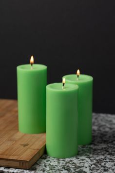 three green candles sitting on top of a wooden cutting board