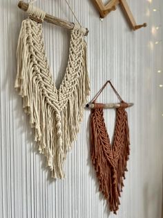 two macrame hangings on a wall next to a wooden hanger with lights