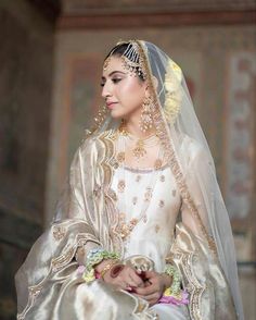 a woman in a white and gold bridal gown with flowers on her head is holding a bouquet