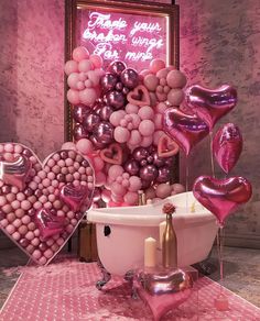 a bathtub filled with lots of pink balloons and heart shaped balloons in front of a sign