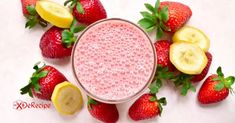 strawberries and lemons surrounding a smoothie in a glass on a white surface