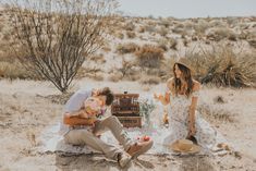 a man and woman are sitting in the desert with an old trunk on their lap