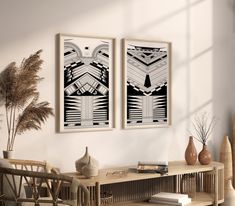 two black and white art prints hanging on the wall next to a table with vases