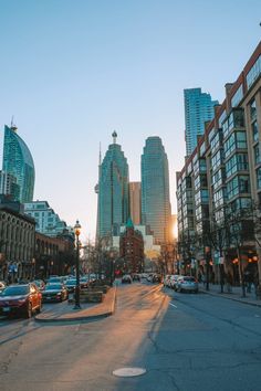 the sun is setting on an empty city street with tall buildings in the back ground