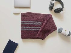 a knitted sweater, headphones, and notebook on a white table with a laptop