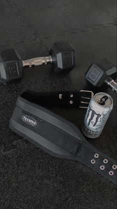 a can of beer and some dumbs are on the ground next to an exercise belt