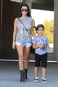 a woman walking next to a little boy wearing black boots and holding the hand of her