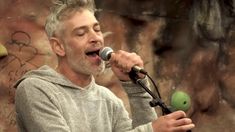 a man singing into a microphone in front of a rock wall