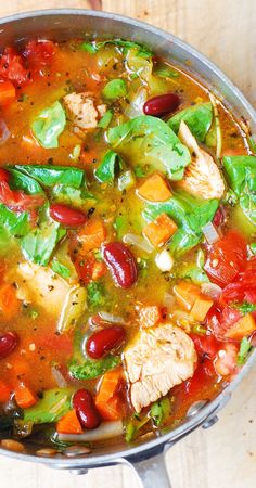 a pot filled with chicken and vegetables on top of a wooden table