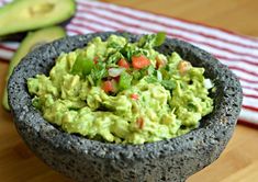 a bowl filled with guacamole sitting on top of a wooden table next to an avocado