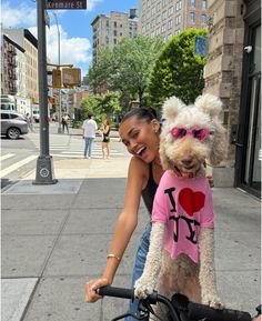 a woman riding a bike with a dog on her back and wearing a shirt that says i love ny