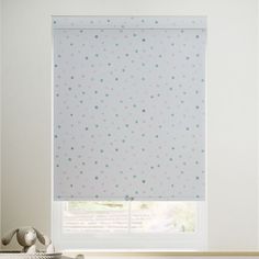 a white window with blue and green polka dots on the roller blind in front of it