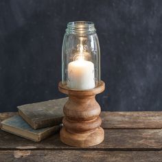 a glass jar with a lit candle sitting on top of a wooden table next to two books