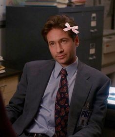 a man wearing a suit and tie with a pink bow on his head sitting in an office