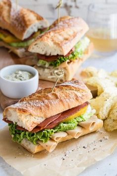 two sandwiches with meat, lettuce and cheese on them next to potato chips