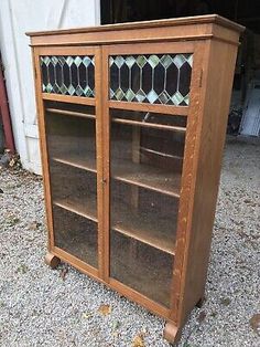 an old bookcase with stained glass doors on the front and bottom shelves is sitting in gravel