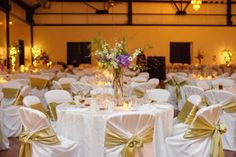 the banquet hall is set up with white linens and gold sashes for guests