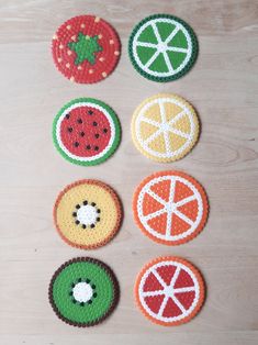 crocheted fruit coasters are arranged on a wooden surface, including oranges, watermelon, and kiwi