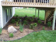 a yard with rocks and plants in the dirt next to a deck on top of a house