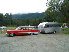 an old red and silver car parked next to a camper trailer in a parking lot