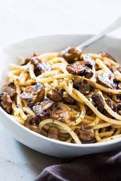 a white bowl filled with pasta and mushrooms on top of a table next to a fork