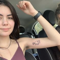 a woman with a pig tattoo on her arm sitting in a car next to another woman