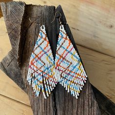 a pair of colorful beaded earrings sitting on top of a piece of wood