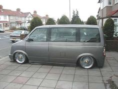 a grey van parked on the side of a road next to a brick sidewalk and houses