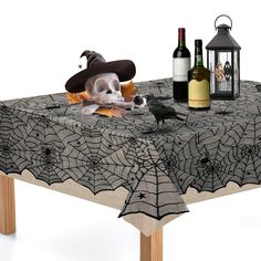 a table topped with a bottle of wine next to a spider web table cloth and a skull wearing a witches hat