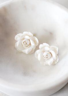 two white flowers sitting on top of a white bowl