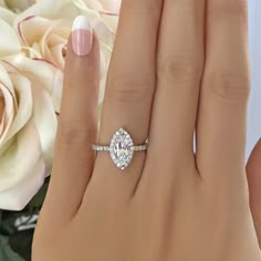 a woman's hand with a diamond ring on it and flowers in the background