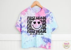 First Grade Vibes!  This direct-to-garment printed design is made from eco-friendly, child safe ink.  This is a cotton candy tie-dye color combination with mostly purple, light blue, and pink. All shirts are custom printed, pressed, and packed in our NJ design studio.  Each shirt is safely pre-treated before printing and will soften with washing. IF YOU NEED YOUR ORDER BY A CERTAIN DATE, PLEASE INDICATE THE DATE NEEDED IN THE MESSAGE TO SELLER SECTION AT CHECKOUT.  DISCLAIMER:  Each tie dye shirt is individually dyed by hand and variations are expected. These variations are a unique and natural part of the dyeing process.   This tie-dye t-shirt style runs a little big, with a slightly boxy, unisex fit. Please see the size chart above. ALL ITEMS ARE PROCESSED IN 3-6 BUSINESS DAYS, NOT INCLU Playful Tie Dye Short Sleeve T-shirt, Playful Tie-dye Short Sleeve T-shirt, Fun Tie Dye Pre-shrunk Top, Fun Pre-shrunk Tie Dye Top, Fun Tie-dye Pre-shrunk Top, Fun Tie Dye Tops With Letter Print, Fun Tie-dye Top With Letter Print, Cute Tie-dye T-shirt With Graphic Print, Cute Tie-dye Graphic Print T-shirt