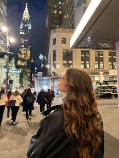 a woman standing in the middle of a busy city street at night with people walking around