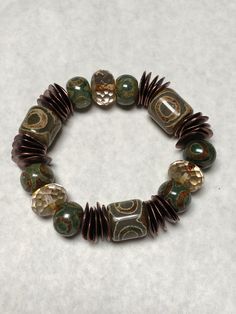 "PRITHVI (Earth Goddess):  This beautiful  bracelet seems so subtle in in its earthy coloring but the large (approx ½\" beads) take it to another level.  Subtle reddish tones to bronze wavy disc mykenos spacers.  Dzi design on barrel beads said to give spiritual protection.  Design includes transparent Picasso Premium Czech faceted rondelles  . . .  very large which \"airs out\" and lightens the pattern.   Strung on high quality pre-stretched elastic cord.  Rolls beautifully on the wrist.   I lo Large Beaded Bracelets, Earthy Brown Beaded Bracelets, Earthy Bronze Beaded Jewelry, Earthy Bracelets, Handmade Brown Nature-inspired Bracelet, Handmade Nature-inspired Brown Bracelet, Earthy Hand-strung Bracelets, Earthy Accessories, Earthy Crafts