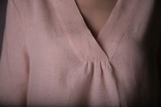 a woman wearing a pink shirt and necklace with an open v - neck, standing in front of a dark background