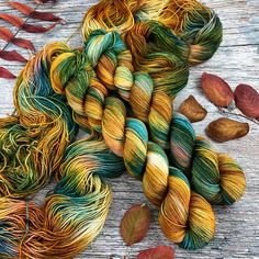 several skeins of yarn and leaves on a wooden surface with autumn foliage in the background