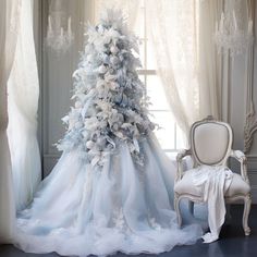 a blue and white christmas tree sitting next to a chair in front of a window