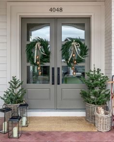 two christmas wreaths sitting on the front door of a house with potted trees