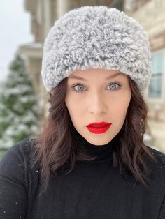 a woman wearing a gray hat and red lipstick in front of snow covered buildings on a winter day