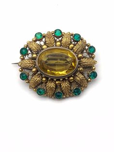 "This brooch is a lovely example of an circa 1890s/1900s Victorian pin design. It is a Victorian metalwork masterpiece with a beautiful rhinestone setting. A large impressive piece, that look amazing worn! This gold filled metal design is richly detailed with fern leaves frame, metal bead work, open work design of the period graceful by green crystals that delineate the outer edge  The 25mmx18mm large topaz, faceted glass rhinestone is in a high bezel, open back setting. Also the 5mm green stone Antique Jeweled Brooch For Wedding, Victorian Jeweled Gold Brooches, Ornate Jeweled Gold Brooches, Ornate Gold Jeweled Brooches, Antique Green Filigree Brooches, Antique Green Brooches For Wedding, Vintage Yellow Brooch Jewelry, Victorian Metalwork, Leaves Frame