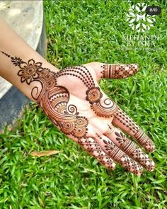 henna tattoo on the palm of someone's hand with green grass in the background