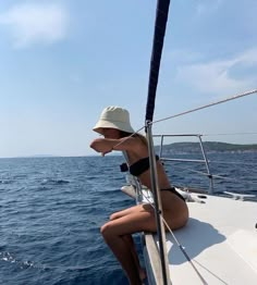 a woman is sitting on the bow of a boat in the ocean, wearing a hat