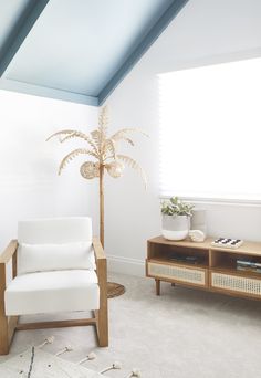 a living room with a white chair and a palm tree in the corner on the wall