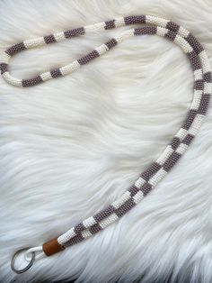 a white and grey leash with wooden handle on top of a fur covered floor next to a keychain