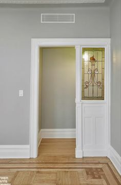 an empty room with white trim and stained glass door on the left, wood flooring on the right